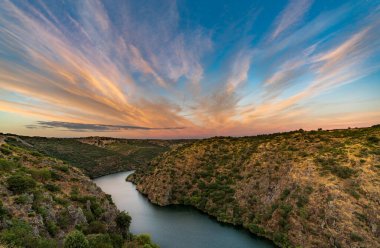 Gün batımında pembe bulutlarla nehir ve kanyon