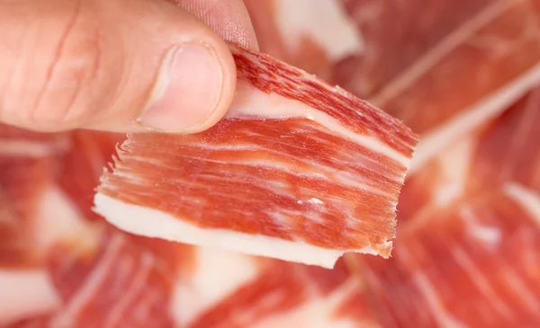 Vue du dessus de la main de l'homme caucasien prenant une tranche de jambon Serrano — Photo