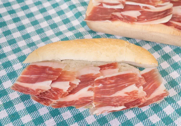 Vista laterale del panino al prosciutto di Serrano sulla tovaglia a scacchi — Foto Stock