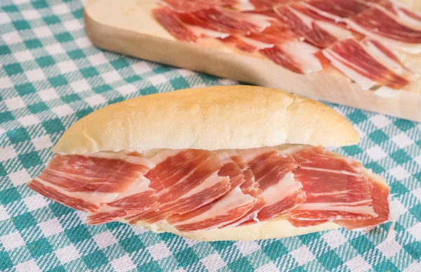 Side view of Serrano ham sandwich over checkered tablecloth — Stock Photo, Image