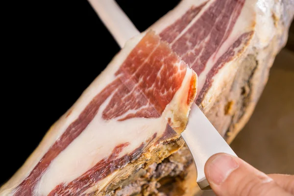 Top view of knife and hand cutting Serrano ham, black background — Stock Photo, Image