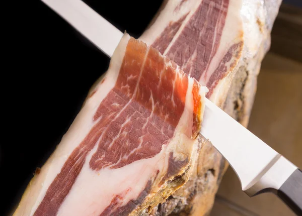 Top view of knife cutting Serrano ham, black background — Stock Photo, Image