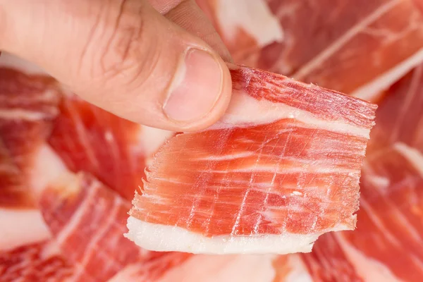 Vue du dessus de la main de l'homme caucasien prenant une tranche de jambon Serrano — Photo