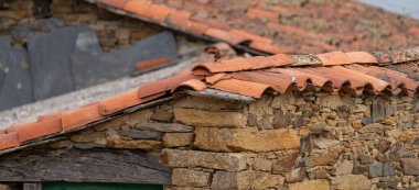 Close-up of a rustic stone house highlighting weathered terracotta roof tiles.
