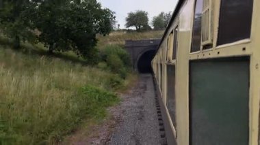 Eskimiş sarı bir kömür treni karanlık bir tünelden çıkıyor ve kamera arka vagonlarını gün ışığına çıkarken yakalıyor..