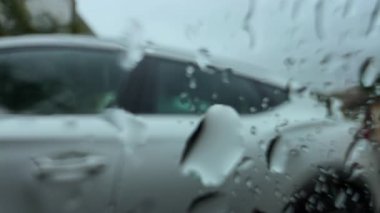 Yağmurlu bir arabanın penceresinden: park etmiş beyaz bir SUV ve sakin, bulutlu bir günde bulanık bir mahalle.