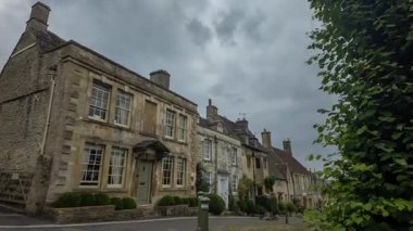 Zaman çizelgesi, İngiltere 'deki Cotswolds taş kulübelerinin dramatik ve bulutlu bir gökyüzünün altında olduğunu vurguluyor..