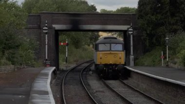 A diesel train arrives at the station in bright daylight, highlighting its movement and mechanical power.