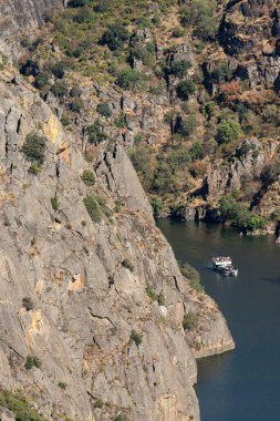 Dar bir nehir boyunca süzülen bir tekne yüksek kayalıklar ve yemyeşil yeşilliklerle çevrili, nefes kesici bir doğal manzara yaratıyor..