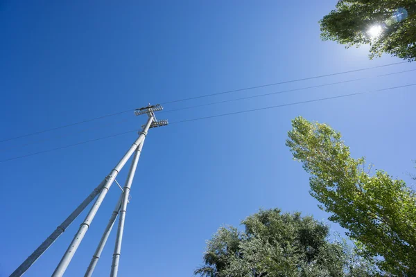 Railway catenary against a blue sky and sun — Stock Photo, Image