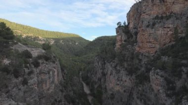 Kireçtaşından bir kanyonun üzerinde hafif bir süzülüş ve kıvrılan bir nehir ışığı, derin gölgeler ve bulutlu mavi bir gökyüzü..