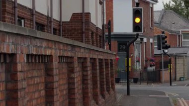 Bükülmüş demir bir direğin üzerindeki İngiliz trafik lambası kehribardan kırmızıya dönerken bir araba geçiyor..