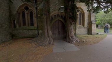 Serene sonbahar sahnesi: olgun ağaçlar, düşen yapraklar ve asfalt bir yol tarafından çerçevelenmiş antik bir Gotik kilise kapısı.