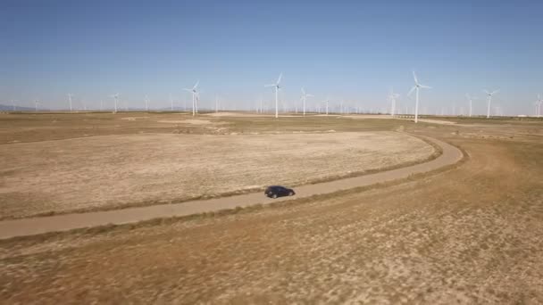 Following a black car in windmill farm, curved road — Stock Video