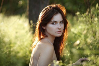 Güneşli bir günde çimenlerde oturan güzel bir kız