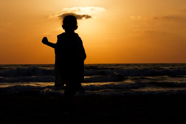 Silhouette of little girl on a beach at sunset — Stock Photo, Image