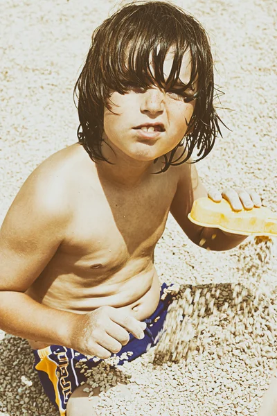 Lindo chico, jugando con guijarros en la playa por la mañana —  Fotos de Stock
