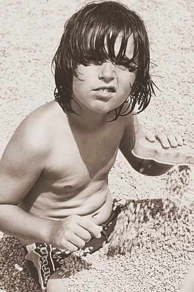 Niedlicher Junge, der morgens mit Kieselsteinen am Strand spielt — Stockfoto