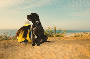 Sahilde oturan bir köpek ile kız