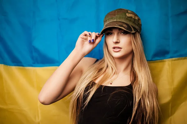 Женщина в шапке цвета хаки против украинского флага — стоковое фото