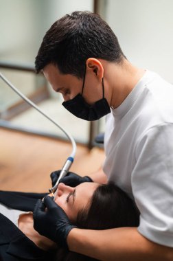 Diş hijyenisti diş temizleyicisi. Hasta sandalyeye yaslanırken vakum kullanıyor. Klinik maskesi takıyor.