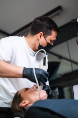 Diş hekimi, el bilgisayarı tarayıcısıyla dijital tarama yapıyor. Hasta, klinik ışığı altında yatıyor.