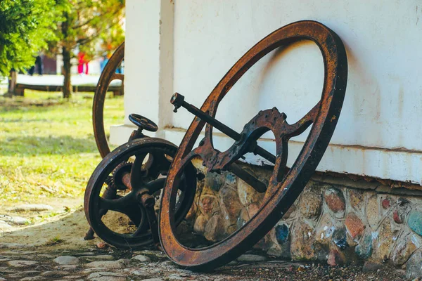 Steel old rusty wheel from agricultural machinery near white wall