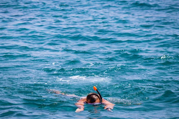 Jovem nada na água azul usando uma máscara com um snorkel para respirar — Fotografia de Stock