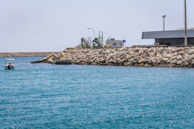 Beyaz bir binası ve suda küçük bir yatı olan taştan bir sahil.