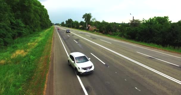 Imágenes aéreas de un coche que monta en una carretera entre campos verdes al atardecer . — Vídeo de stock