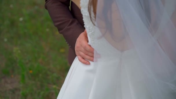 Un uomo abbraccia una donna per la vita, lo sposo tiene le mani sui fianchi della sposa, scene d'amore, giovani felici, un vestito bianco, un bel vestito da vacanza. — Video Stock