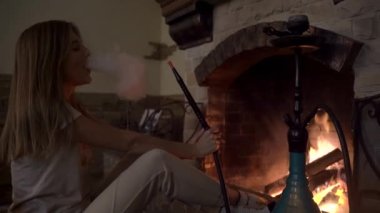 Şöminenin yanındaki karanlıkta nargile içen bir kızın silueti.