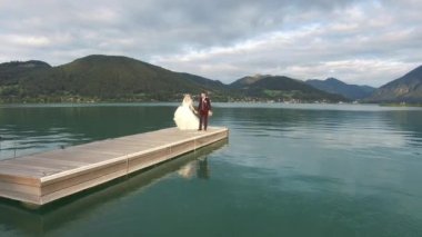 Boho tarzında gelin ve damadın göl kıyısındaki iskelede kucaklaşması.