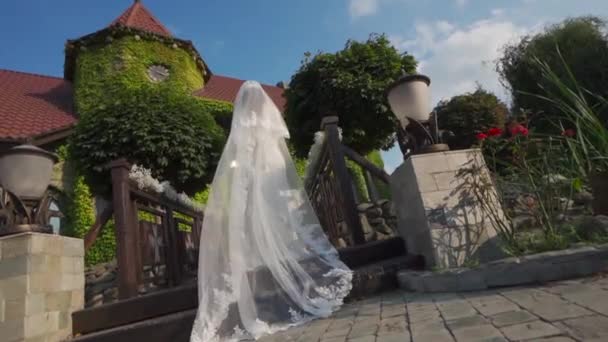 Noiva em um vestido bonito sobe para a ponte, contra o fundo de um belo castelo verde coberto com vegetação — Vídeo de Stock