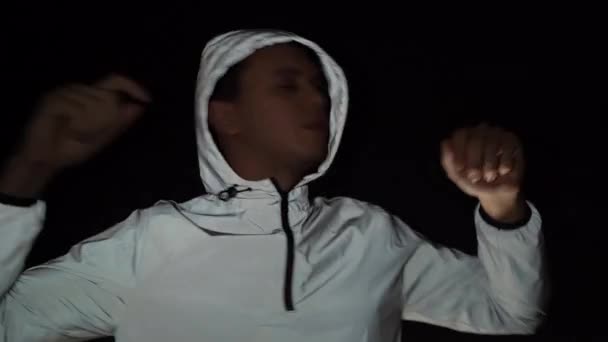 Fešák šťastný chlap tančí na černém pozadí v reflexní bundě, fotografoval paparazzi — Stock video