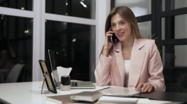 Ofisin içinde akıllı telefondan konuşan kendine güvenen bir iş kadını. Telefon görüşmesi sırasında iş belgelerine bakan profesyonel bir kadın. Uzak işyerindeki kağıtlarla çalışan iş kadını.