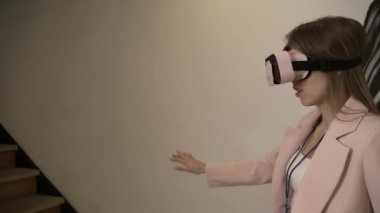 Oturma odasında sanal gerçeklik gözlüğü kullanarak modern oyunlarda oynayan genç bir kız. Geleceğin VR AR modern teknolojilerini kullanarak evde çevrimiçi eğitim. Mutlu tatlı kadın 3D VR kullanarak bir şeye dokun.