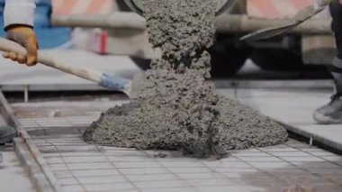 Tanınmayan iki işçi, kanalizasyon borularını taze betonla kaplıyor. Tanınmayan müteahhitler bir inşaat alanındaki büyük bir mikserden dökülen taze betonla bir siperi dolduruyorlar..
