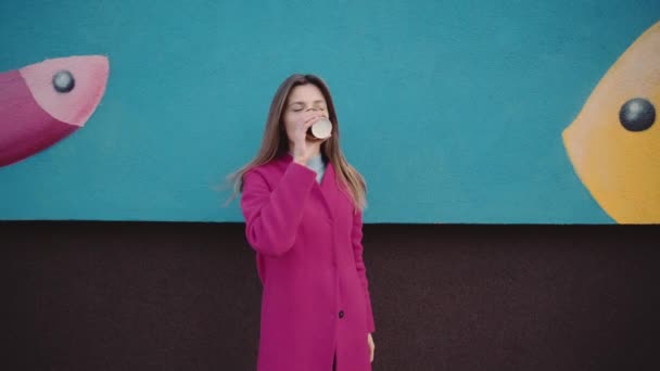 Een meisje in een roze jas drinkt koffie en strekt het uit naar de camera — Stockvideo