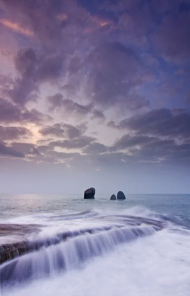 Alba paesaggio dell'oceano con onde nuvole e rocce Foto Stock Royalty Free