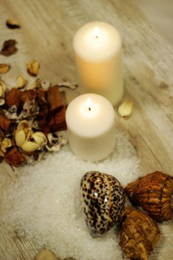 İki mum kabuğu, çakıl taşı deniz tuzu ve çiçek aromalı ahşap masa.