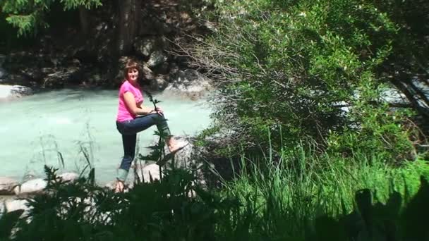 Una giovane donna si trova sulla riva di un fiume di montagna, il sole splende — Video Stock