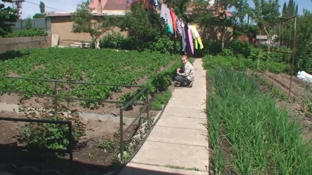 Мальчик сидит на дорожке в огороде — стоковое видео