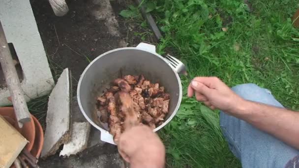 Мужчина на корточках жарит мясо металлическими прутьями — стоковое видео