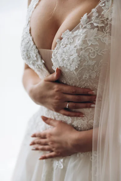 Vacker brud på en grå bakgrund. På kvinnan är en lång bröllopsklänning med spets och öppen rygg. Bukett i händerna. — Stockfoto