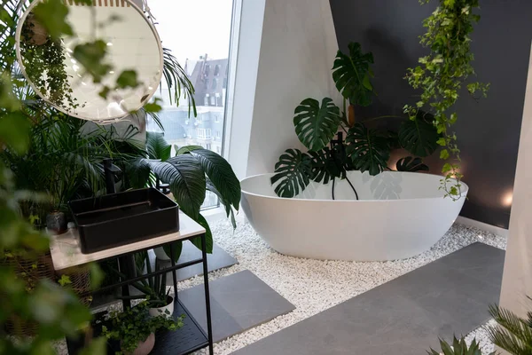 Bright bathroom with subway tiles and a large variety of green potted plants such as a pancake plant and swiss cheese plant creating a green oasis