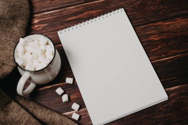 Bilgisayarın üstünde boş not defteri ve ofis tahtasının üzerinde kahve fincanı.