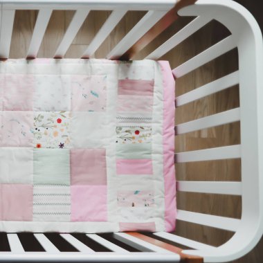 Pembe battaniyeli rahat bir bebek karyolası. Çocuk yuvası için yatak ve tekstil. Pembe ve beyaz bebek beşiğinin fotoğrafı.