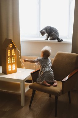 Evdeki rahat oturma odasında kediyle oynayan bir kız. Çocuk evcil hayvanlarla oynuyor. Çocuklar ve evcil hayvanlar. Samimi sıcak görüntü, hygge biçimi