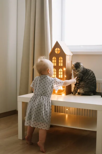 Girl playing with cat in cozy living room at home. Kid play with pets. Children and domestic animals. Cozy warm image, hygge style — Stock Photo, Image